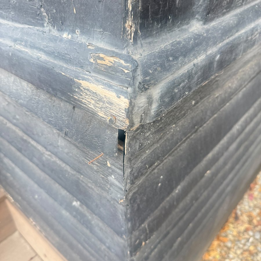 Close-up of peeling black paint on wood siding before repainting