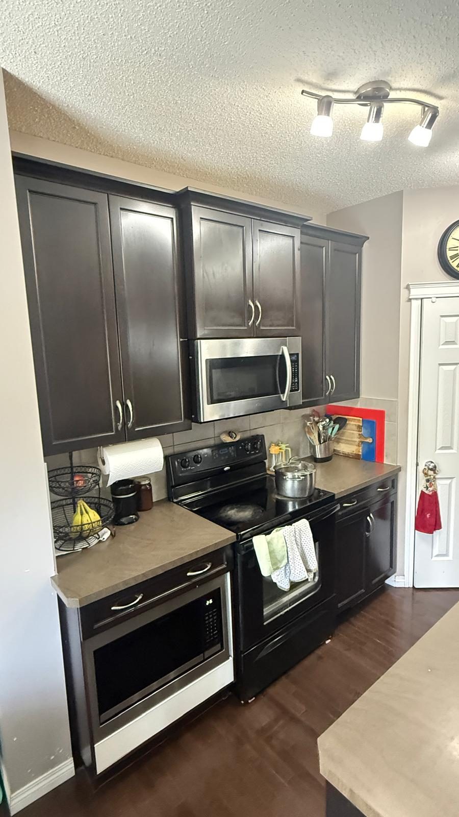 Dark espresso kitchen cabinets and range wall before refinishing in Kincora, Calgary