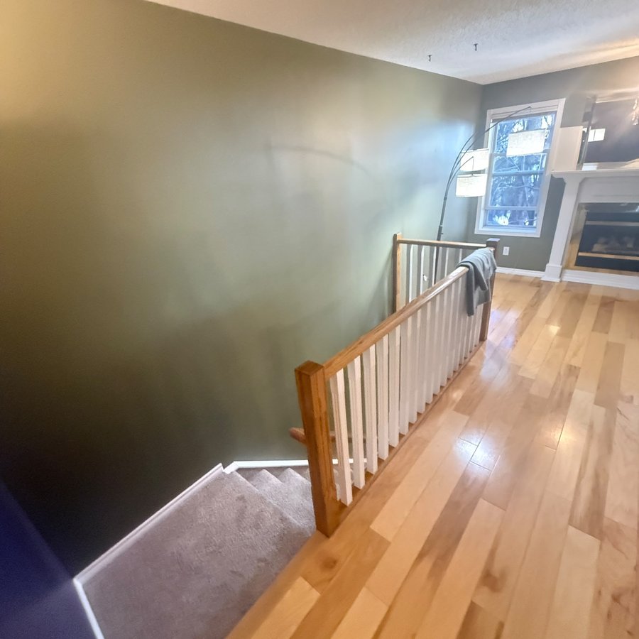 Living room and tall stairwell wall in dark olive before repainting in Mount Pleasant, Calgary