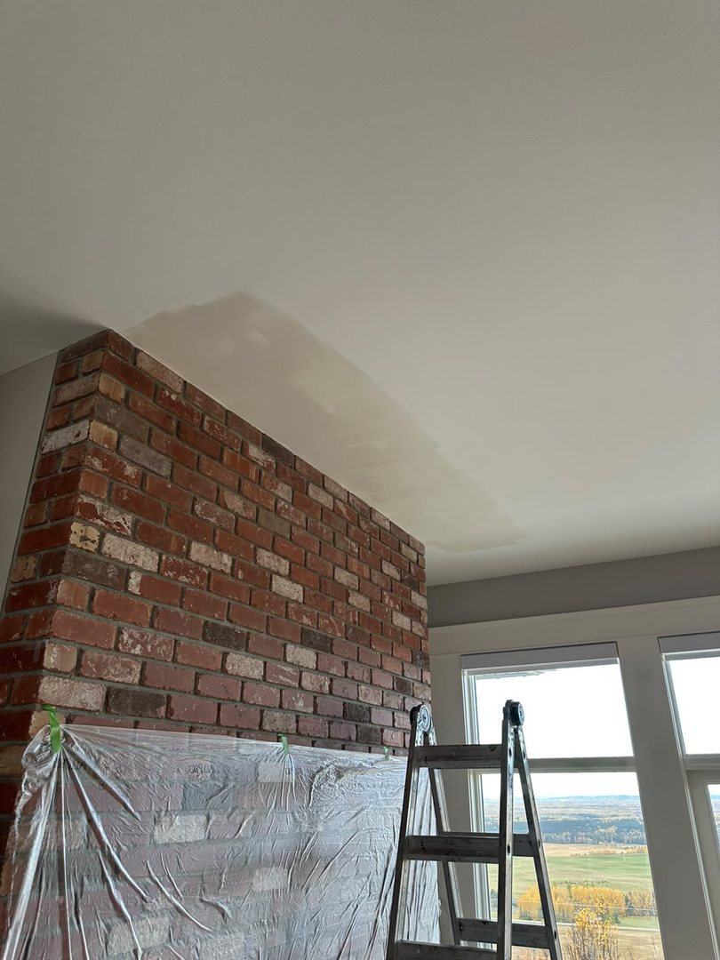 Freshly mudded ceiling repair drying beside a brick chimney in Rocky View County, Alberta