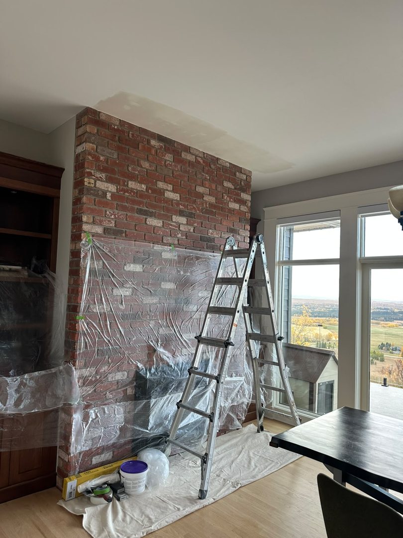 Ceiling repair work in progress with ladder and drop cloths protecting a brick fireplace in Rocky View County, Alberta