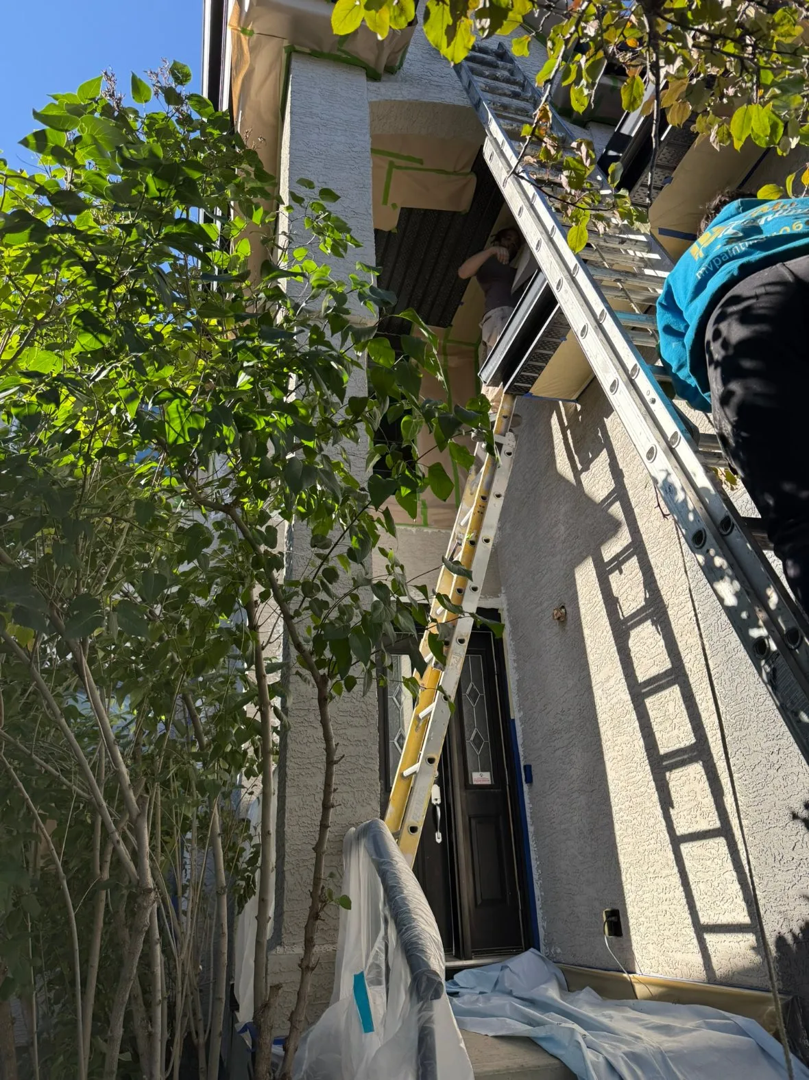 Painter on a ladder painting a stucco house exterior in Calgary